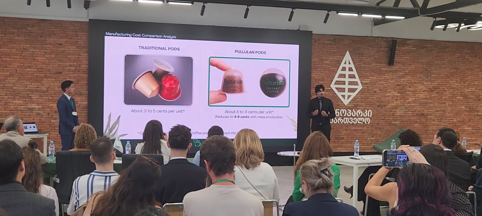 Manufacturing cost comparison slide, traditional pods against pullulan pods, on stage at the SAGE World Cup